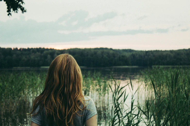 there is a woman sitting by the water watching the sunset