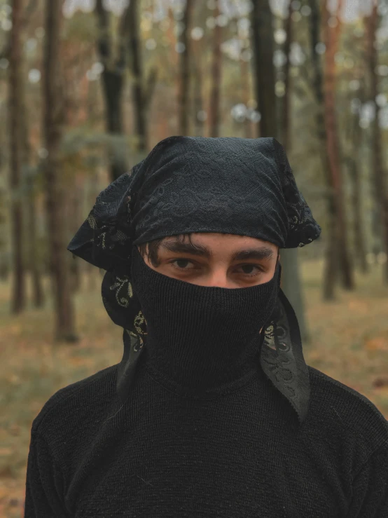 a man in black is wearing a mask in front of trees