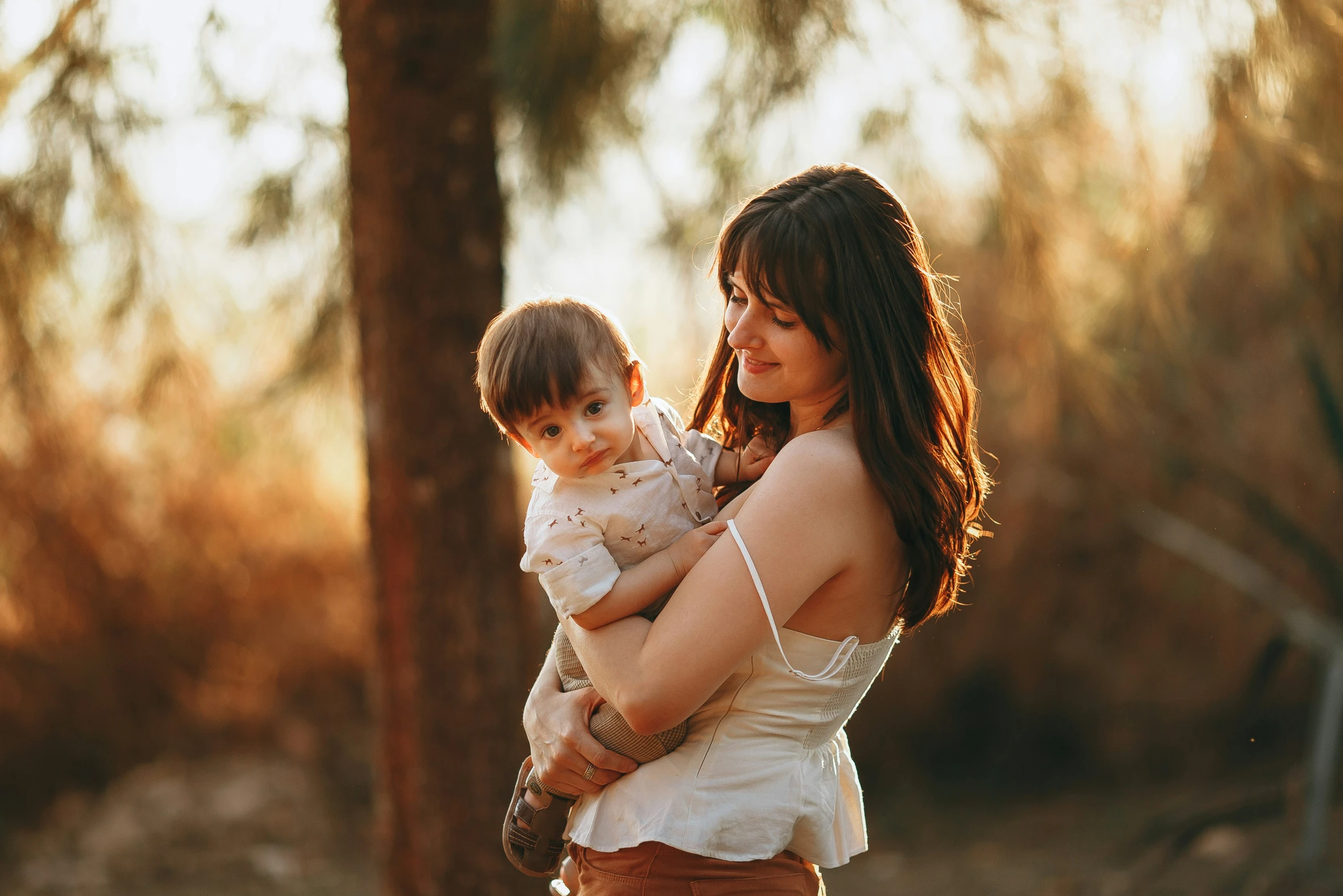 a woman holding a baby in her arms in front of a tree