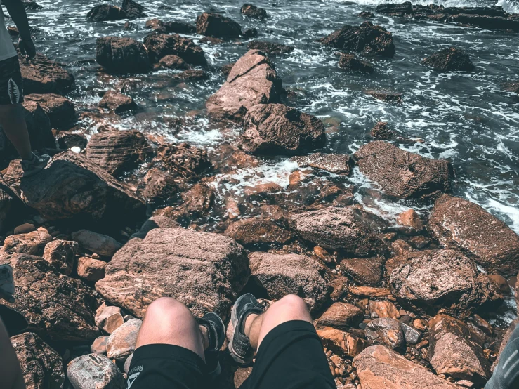 a person in black pants and sneakers sitting on rocks near the ocean
