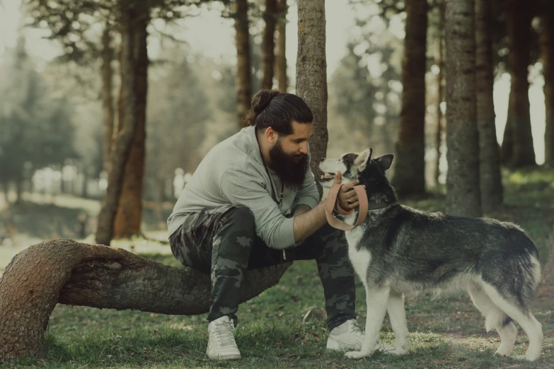 a man with a beard petting a dog in the woods