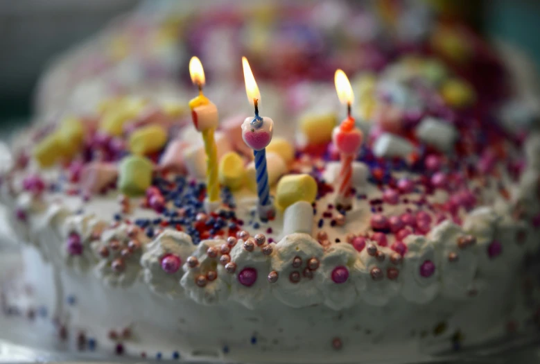 cake with white frosting and brightly colored toppings with seven lit candles
