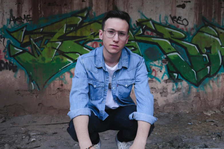 a man kneeling down in front of a wall with graffiti