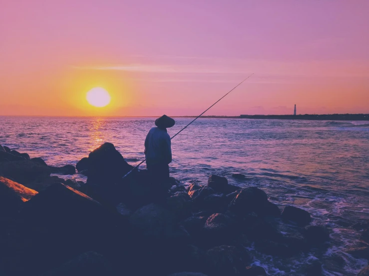 a man fishing in the ocean at sunset