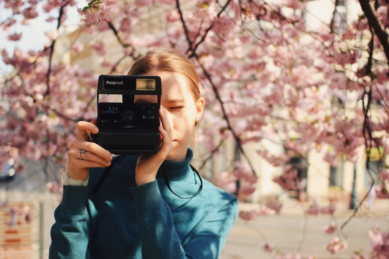 a girl holds a camera in front of cherry trees