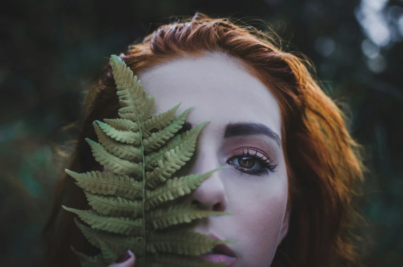 a woman holds a green plant to her face and looks at it