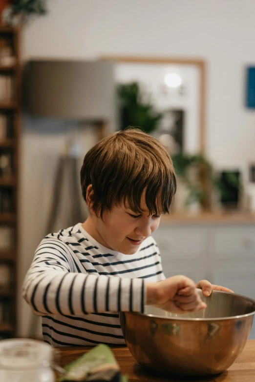 a boy holding a bowl while sitting at the table