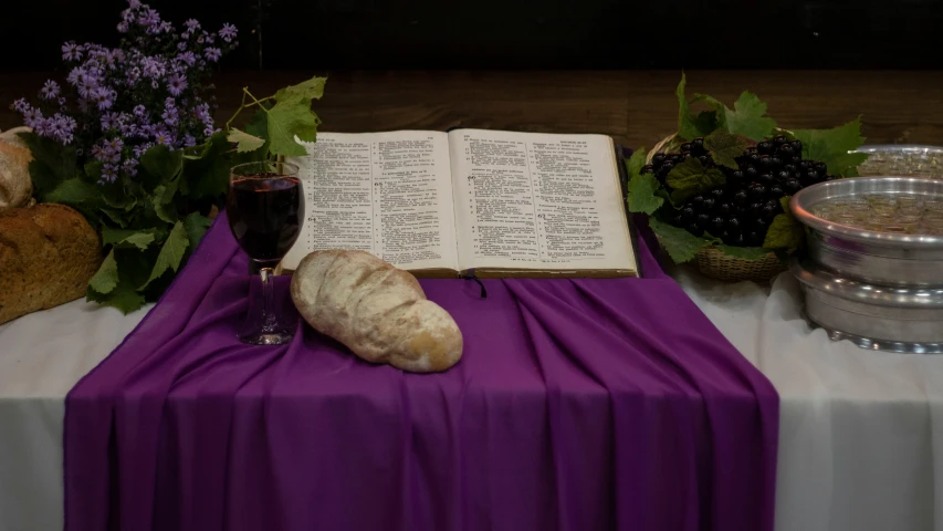 an open book, a glass of wine and some bread on a table