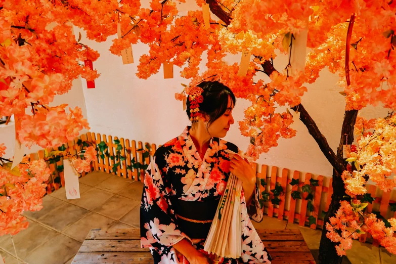 an asian woman in kimono is sewing under a red tree