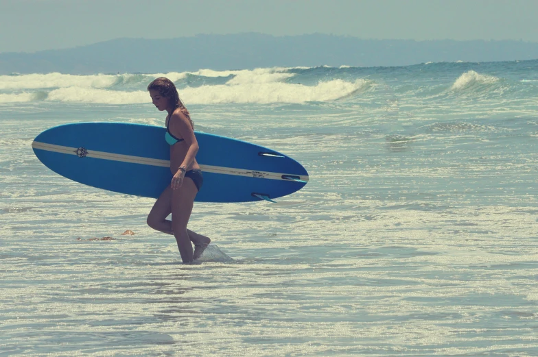 a woman with a blue surfboard walking out of the ocean