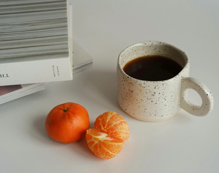 an orange sitting beside a cup of coffee next to a book