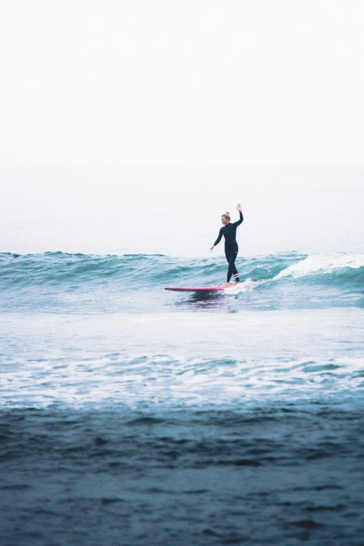 person on surfboard with arms outstretched riding small wave