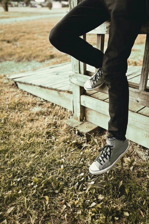 man's feet in sneakers leaning against the side of a wooden platform