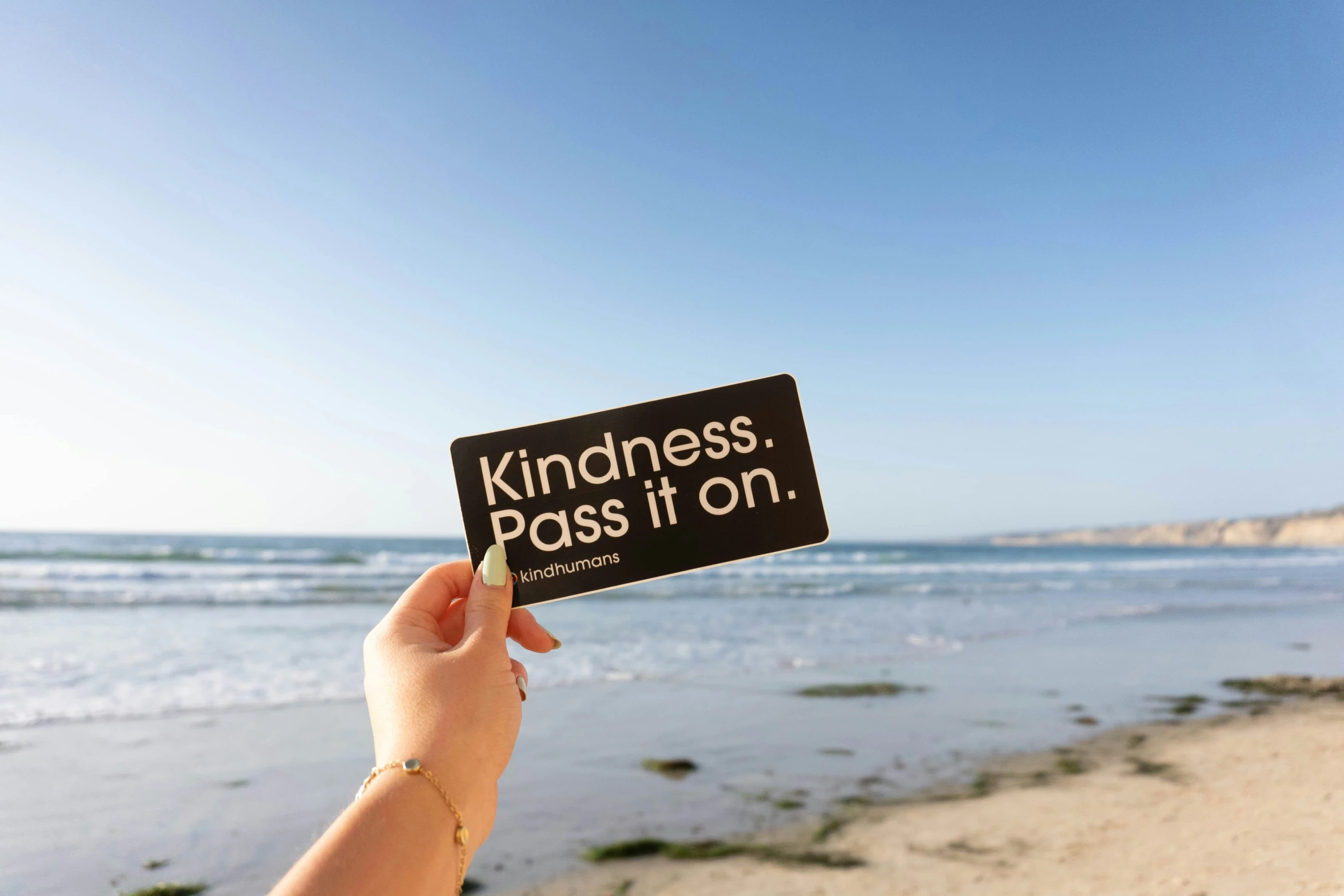 someone holding up a card saying kindness and looking out to the ocean