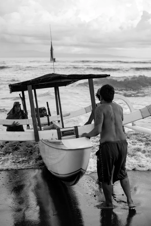 black and white pograph of s on the beach near an old boat