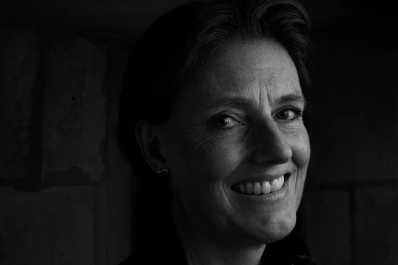 black and white pograph of a smiling woman in front of a wall