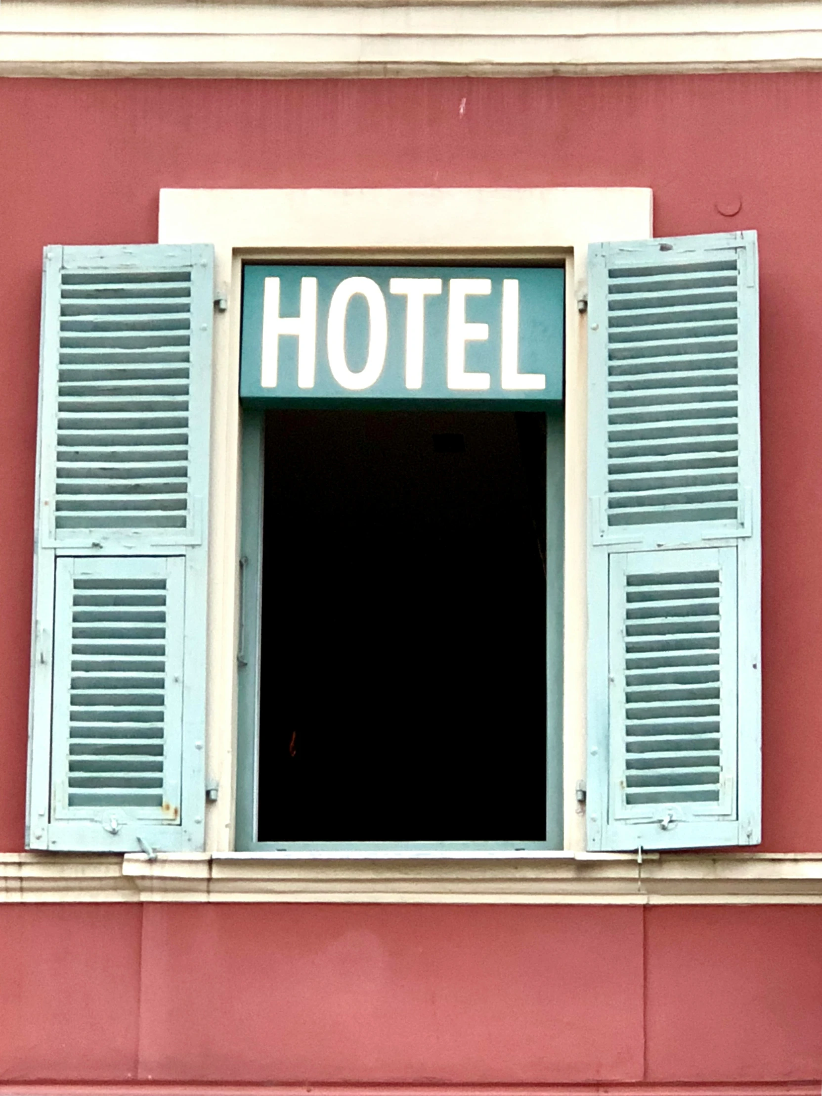 blue window with shutters on the side of a pink building