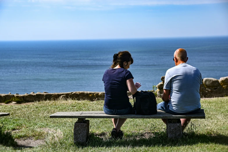 two people sit on a bench and stare at the water