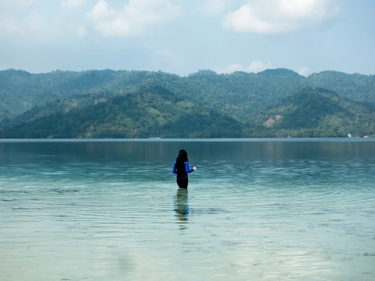 a woman is in the water, with mountains in the background