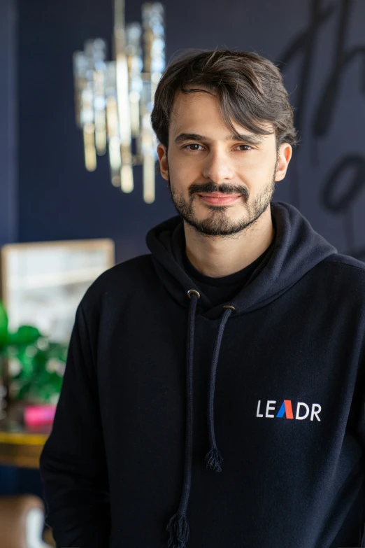 a man is wearing a leader hoodie standing by the chandelier