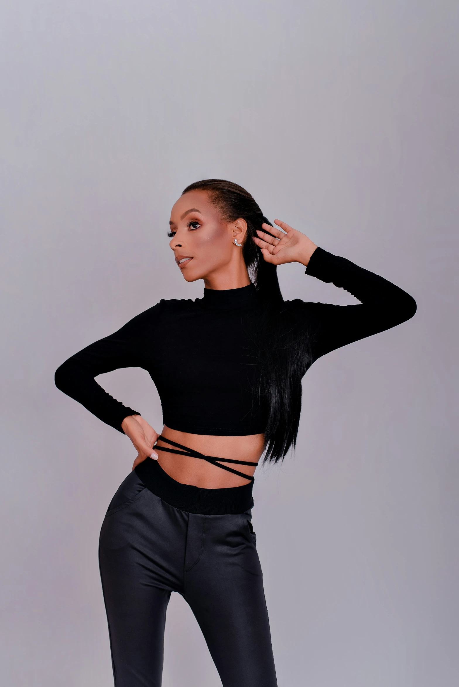 a woman in tight black pants and a crop top is looking off into the distance