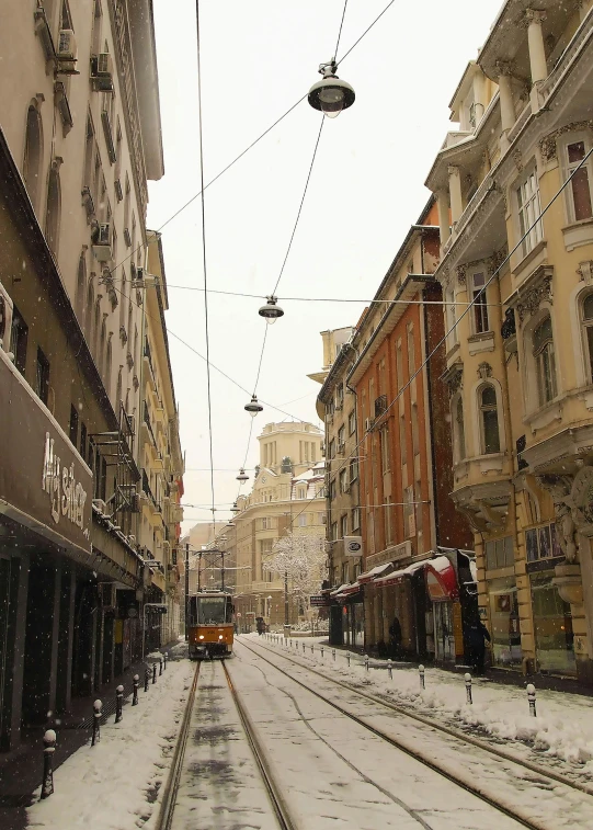 a street covered in snow with a train coming down the track