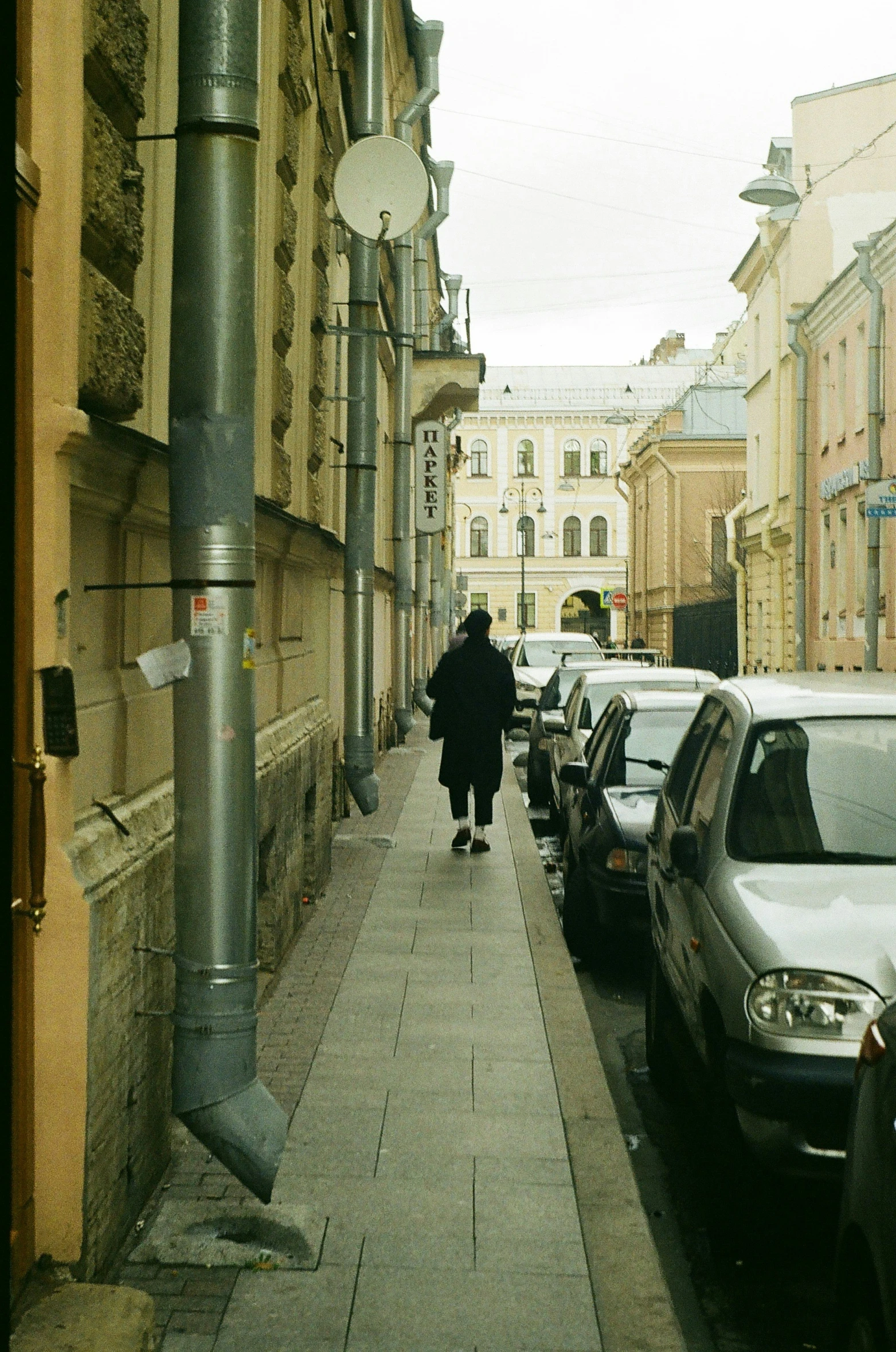 woman in coat walking down an alley next to cars