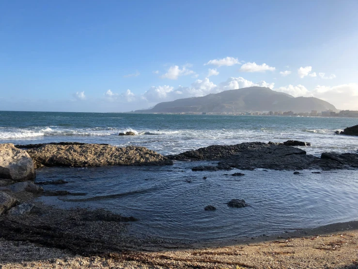 a blue sky and ocean with rocks at the beach