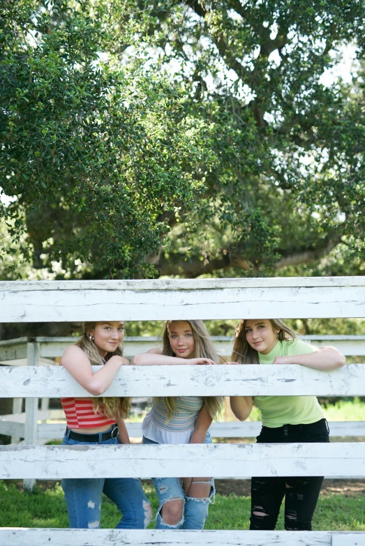 two girls are leaning up on a fence