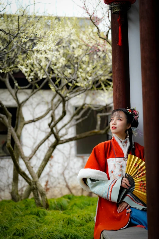 girl in red with fan by wooden pillar