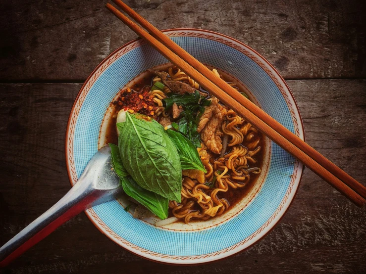 a bowl of noodles with green leaves on a wooden table