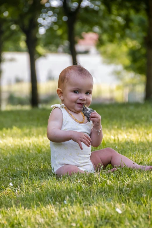 a baby sits in the grass and holds a toy