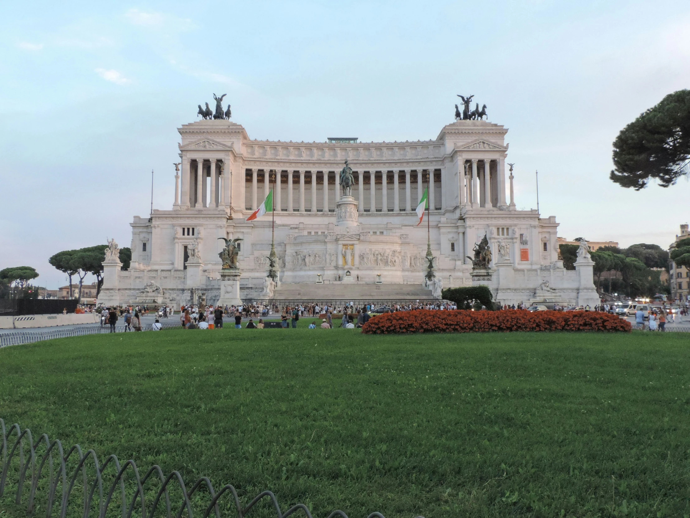 people are standing outside a white building with statues