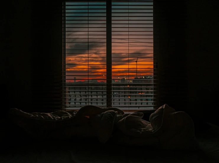 a bed and window with blinds covered in a blanket