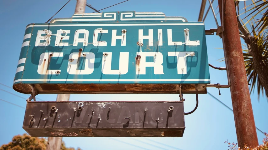 a sign in front of palm trees reads beach hill court