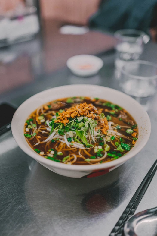 a soup bowl on top of a counter filled with noodles, meat, and vegetables