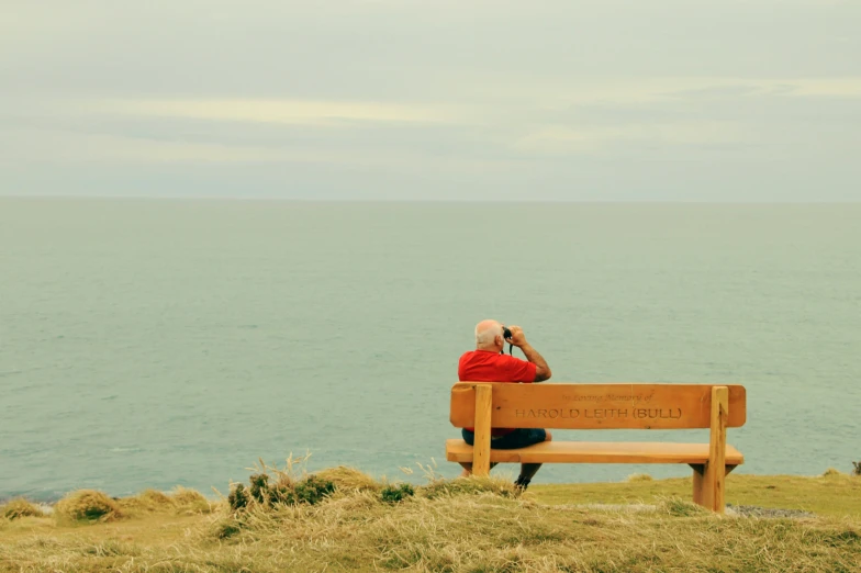 a man in red sits on a bench by the sea