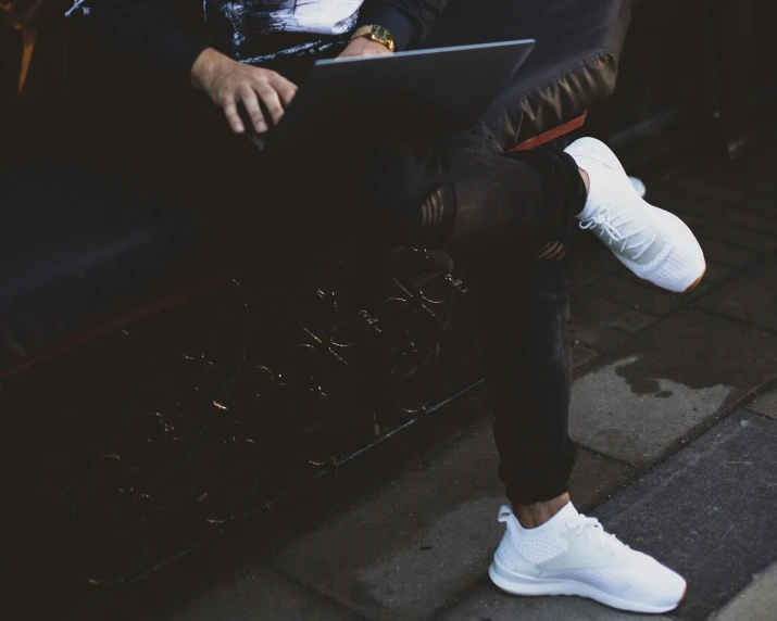 a man with a laptop sits on the sidewalk