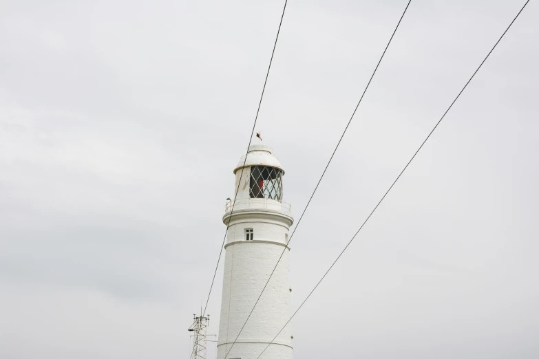 an electric wire above the white lighthouse with the clock