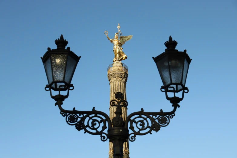 a gold - toned lamp post with statues on the top