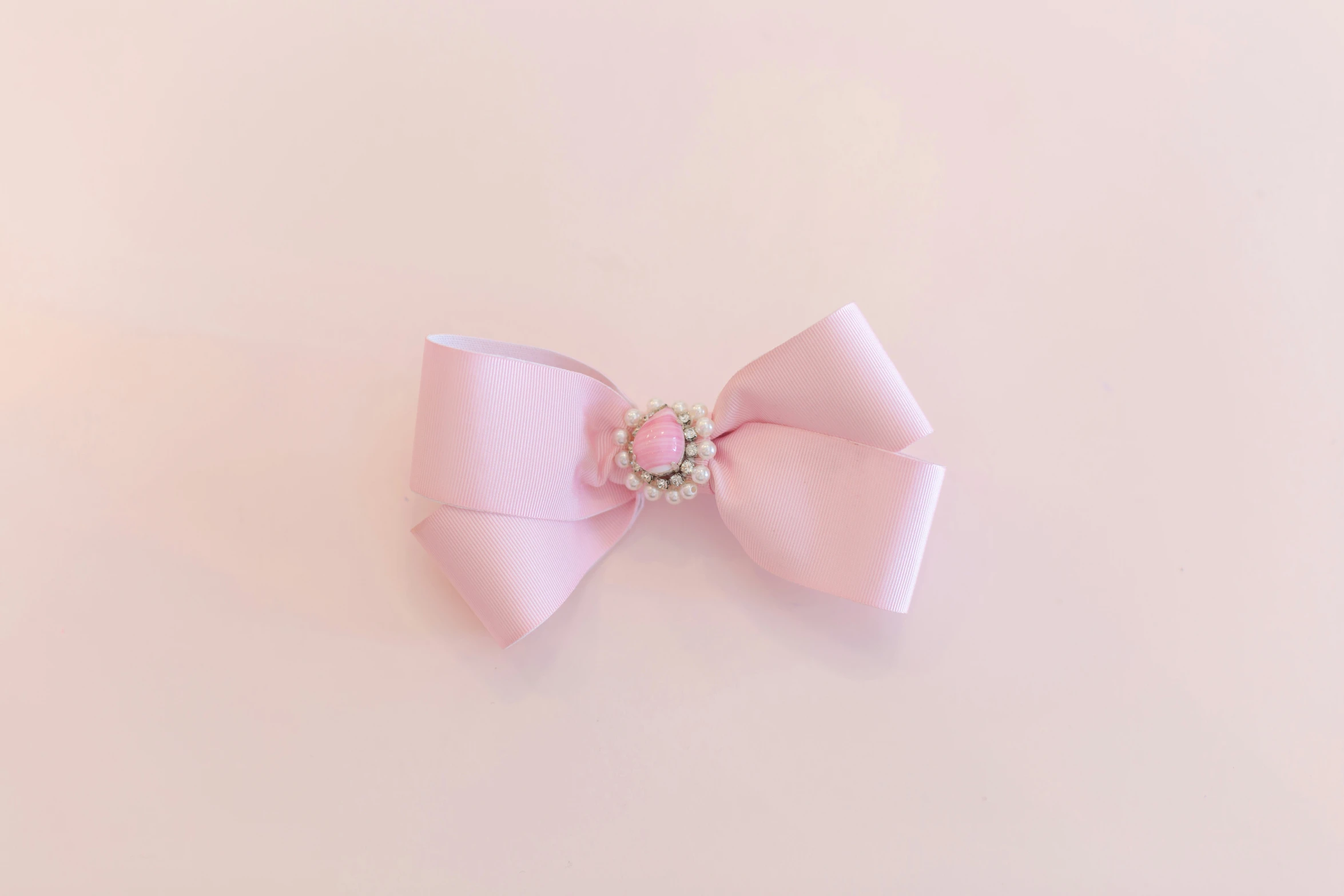 a pink bow with a diamond center sits on a pink surface