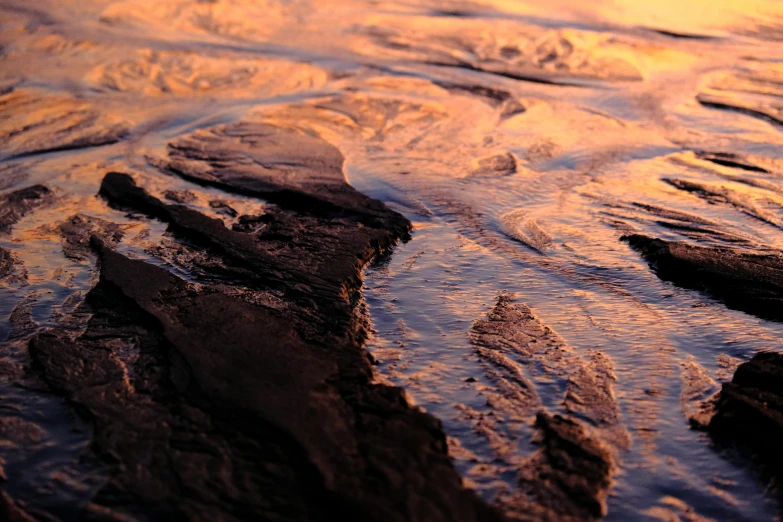 rocks and sand with some water rushing over them