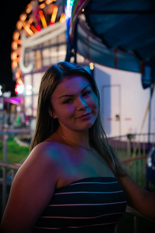 a woman standing by a carnival rides wheel at night