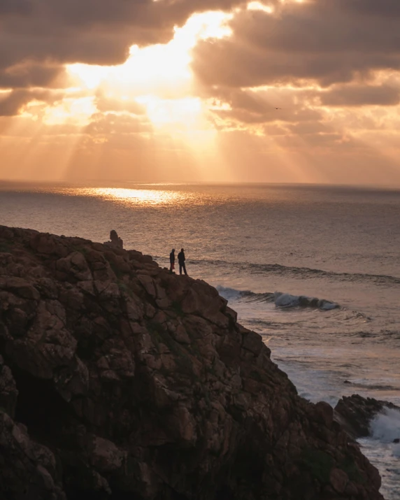 two people are standing on a large rock near the water