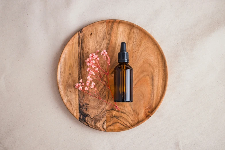 a bottle on a wooden coaster with a pink plant