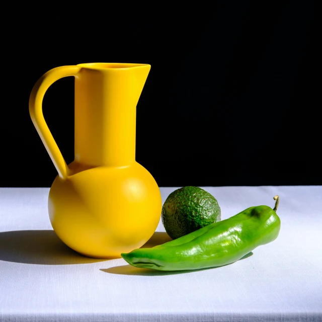 a large yellow glass and a small green pepper on a white table