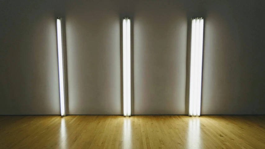 four light poles against a white wall, with light shining in