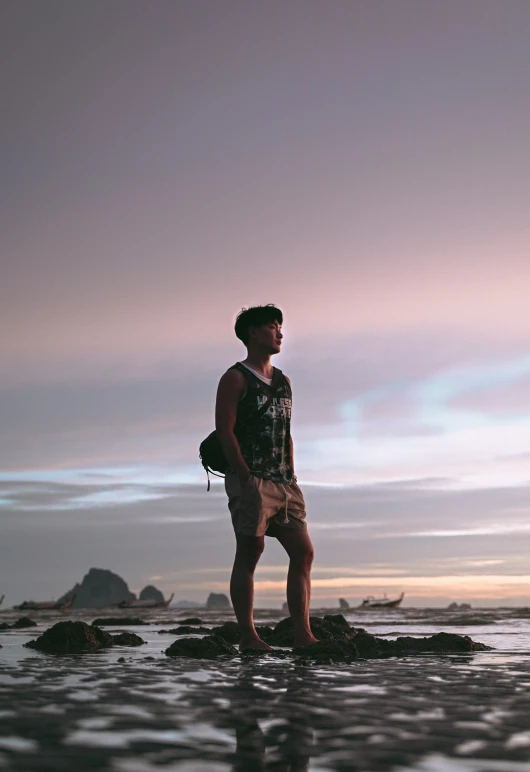 a man standing on rocks at the beach while staring out to sea