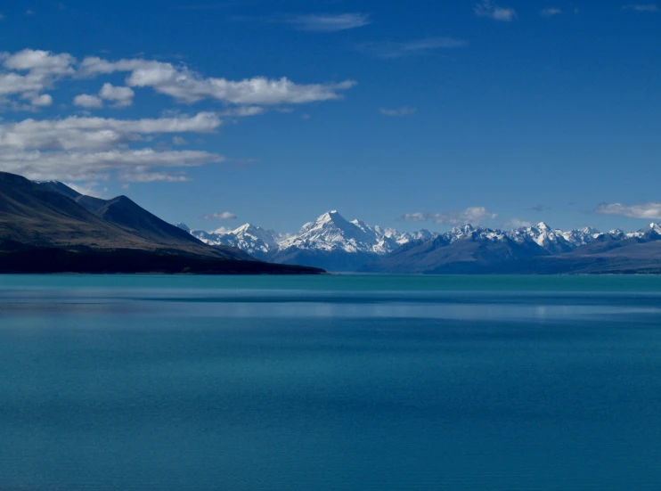 a blue body of water sitting under snow covered mountains