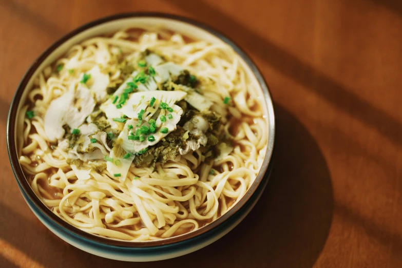 a bowl of noodles with sauce and garnishes on a wooden surface